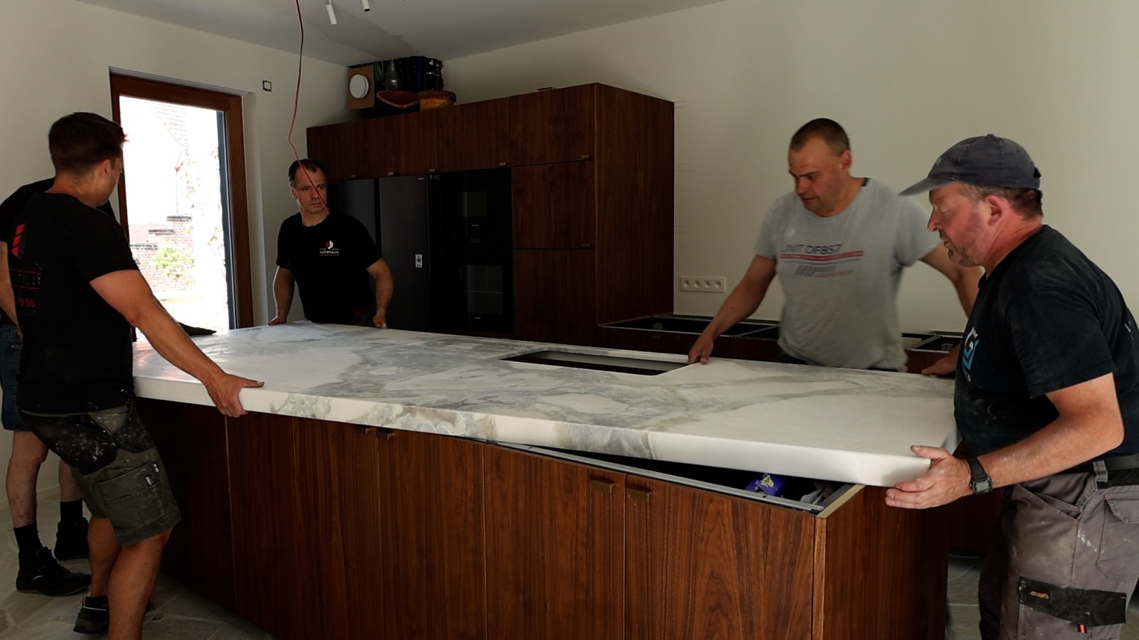 Drie plaatsers leggen een marmeren werkblad op een keukeneiland